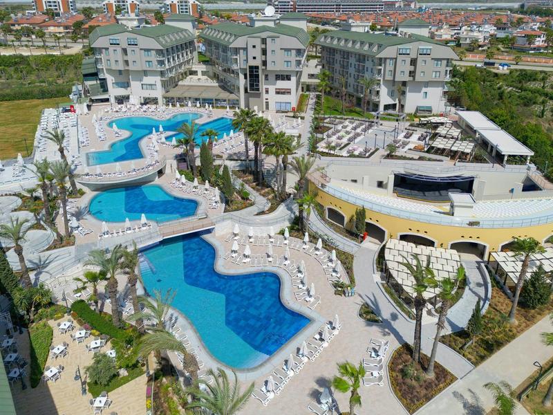 Velký hotelový komplex s několika bazény, palmami a lehátky na slunném místě.