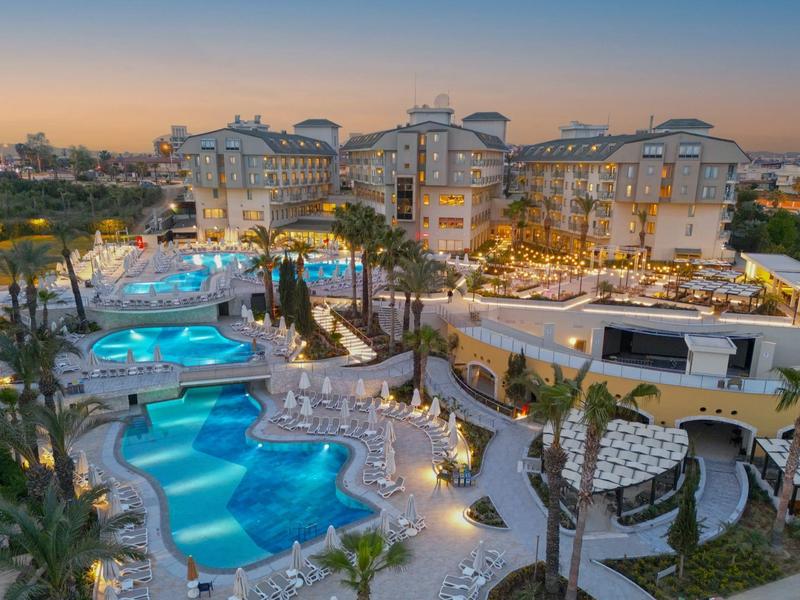 Luxusní hotel s několika bazény a osvětleným venkovním prostorem za soumraku.