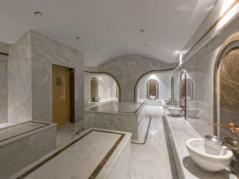 Moderní spa prostor s umyvadly, zrcadly a mramorovými stěnami.