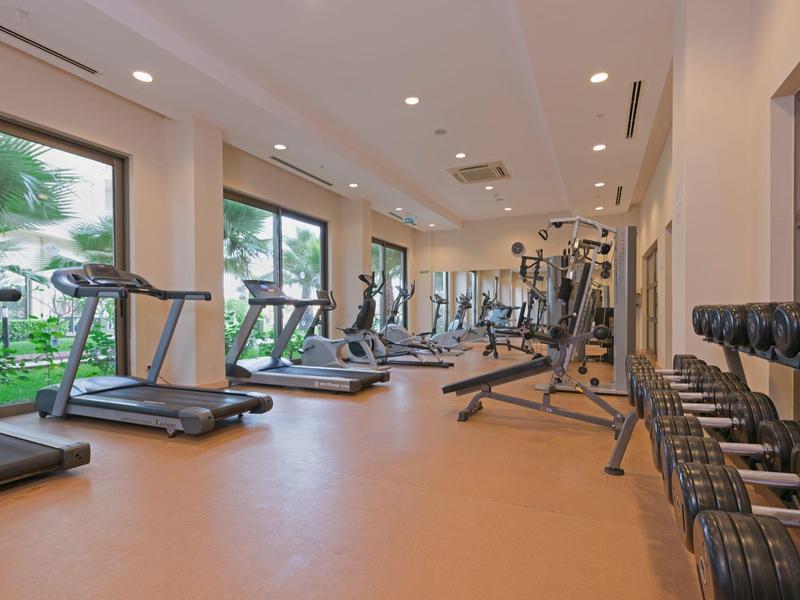 Světelná posilovna s běžeckými pásy, činkami a velkými okny s výhledem do zahrady.