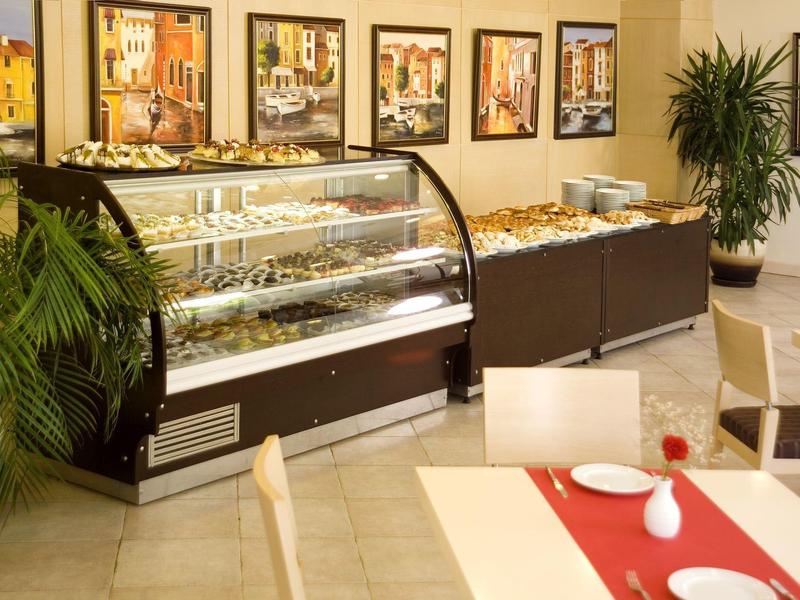 Moderní kavárna s vitrínami plnými pečiva a dekorativními rostlinami.