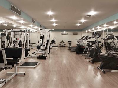 Großer Fitnessraum mit vielen Trainingsgeräten, Holzboden und heller Deckenbeleuchtung.
