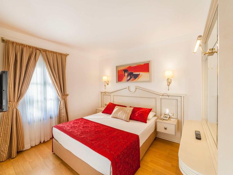 Habitación de hotel acogedora con cama doble, detalles rojos y cortinas a la luz del día.