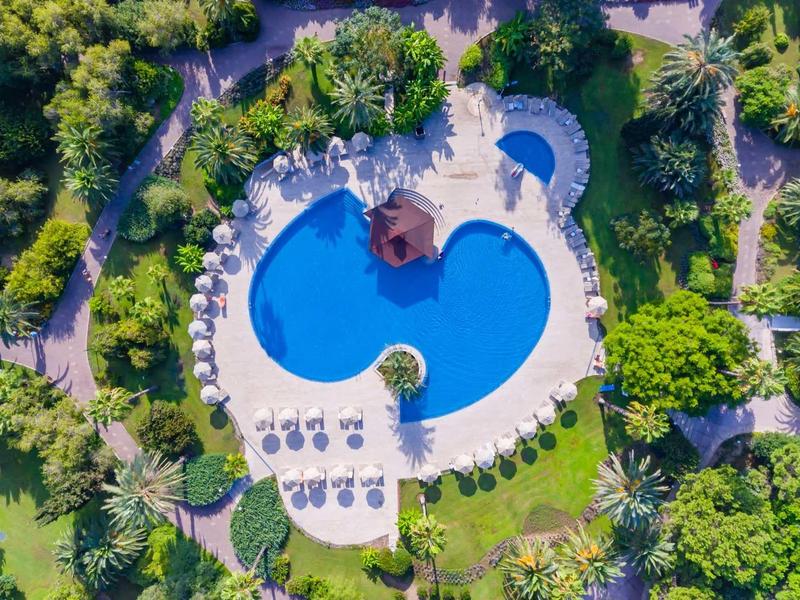 Vista aérea de una piscina azul en forma de corazón en un complejo hotelero verde con tumbonas.