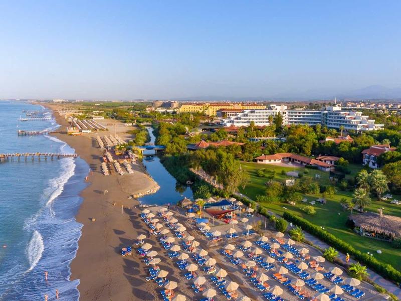 Vista aérea de una playa con sombrillas y un pueblo costero bajo un cielo despejado.
