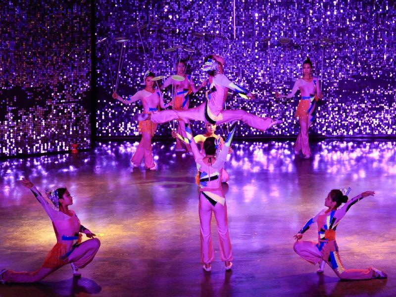 Patinadores sobre hielo iluminados con colores brillantes realizan una actuación en una pista reflectante.