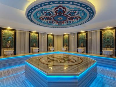 Modern hammam turco con bacino in marmo illuminato e soffitto decorato.