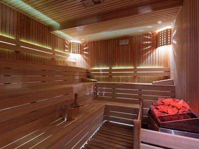 Sauna luminosa in legno con panche e stufa con pietre rosse.