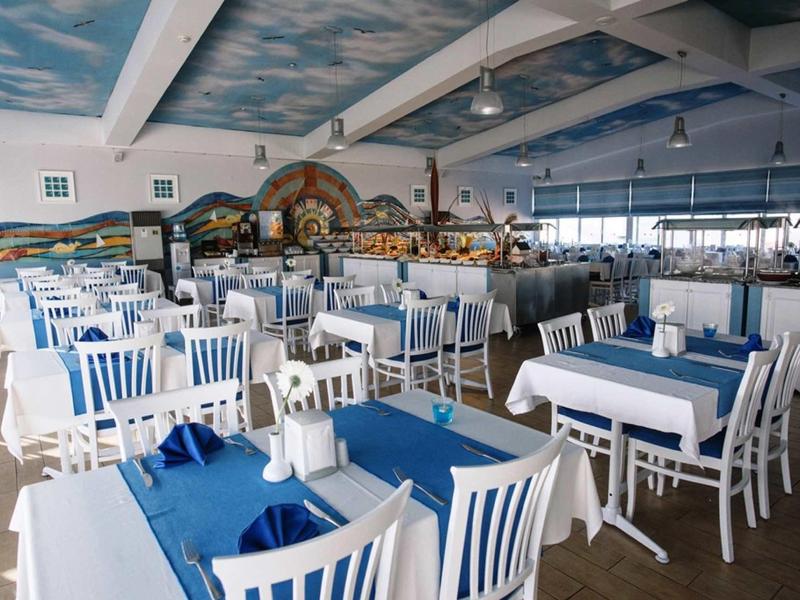 Interno di un ristorante luminoso con sedie bianche e tovaglie blu.