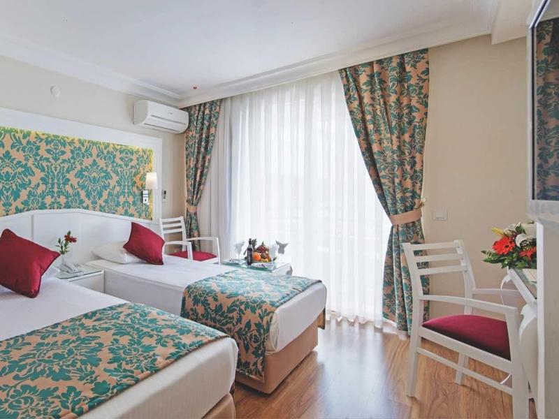 Camera d'albergo con due letti matrimoniali, motivi floreali, pavimento in legno e scrivania vicino alla finestra.