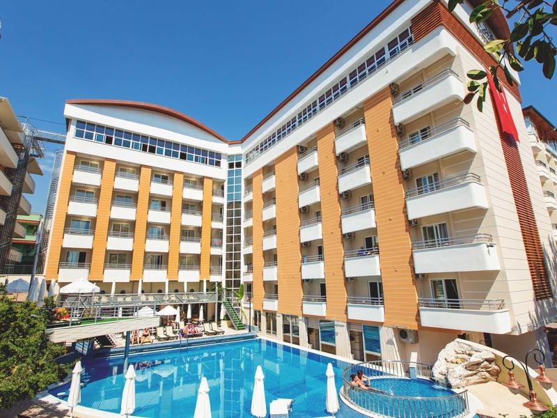 Complesso alberghiero moderno con piscina all'aperto e ombrelloni in una giornata soleggiata.