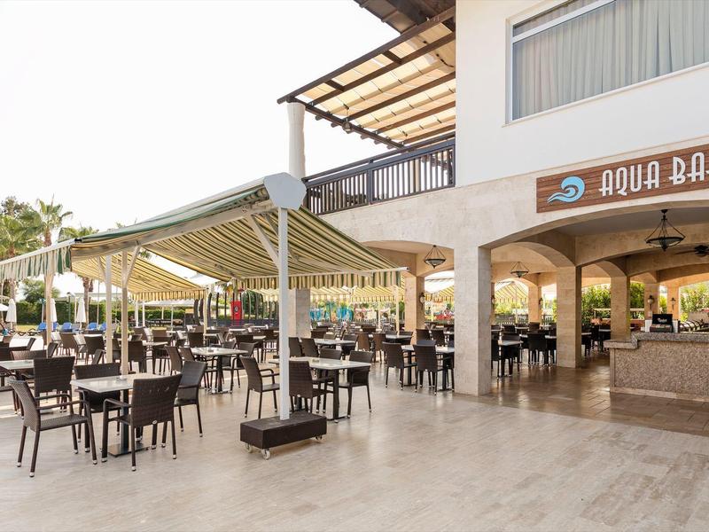Área al aire libre con mesas y sillas junto a un bar en un hotel durante el día.