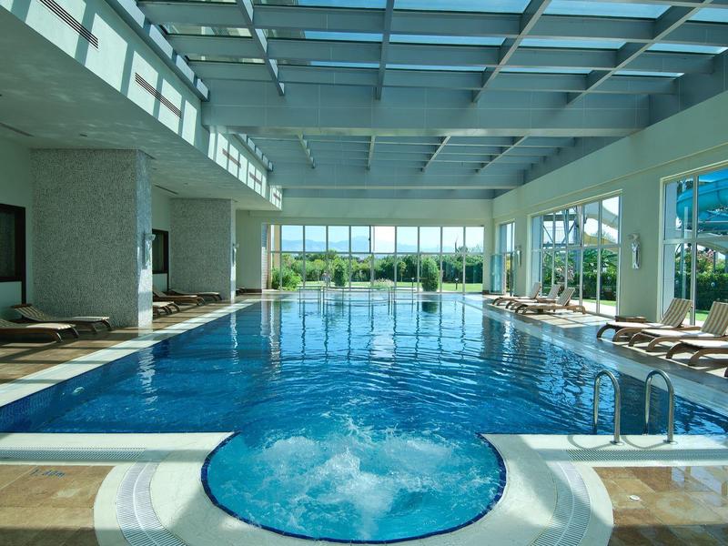 Piscina cubierta bien iluminada con jacuzzi y grandes ventanales con vistas a la naturaleza.