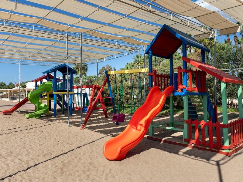 Gran área de juegos con toboganes y estructuras coloridas bajo sombra en un hotel.