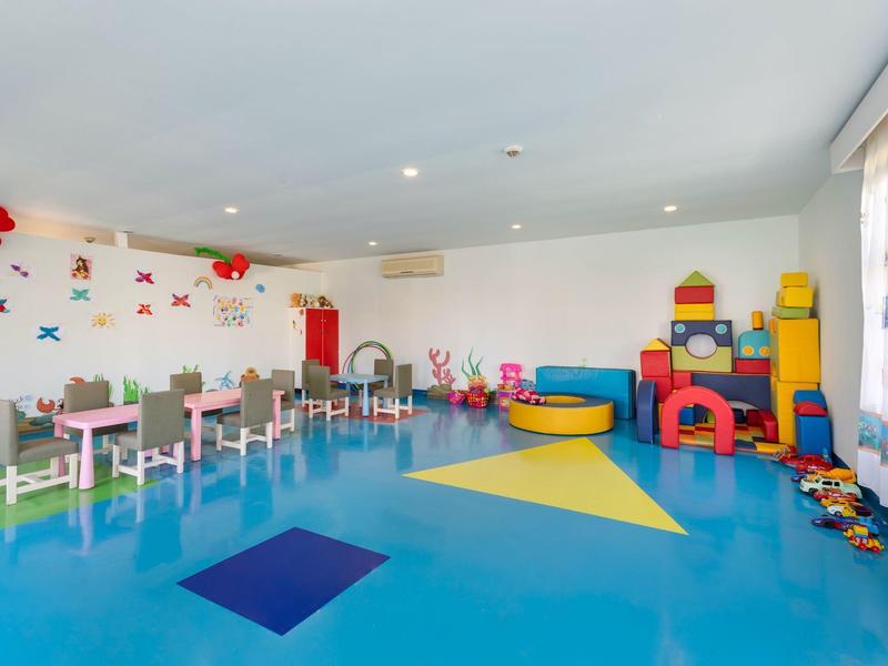 Sala de juegos colorida y moderna con mesas, sillas y juguetes en un espacio luminoso con suelo azul.