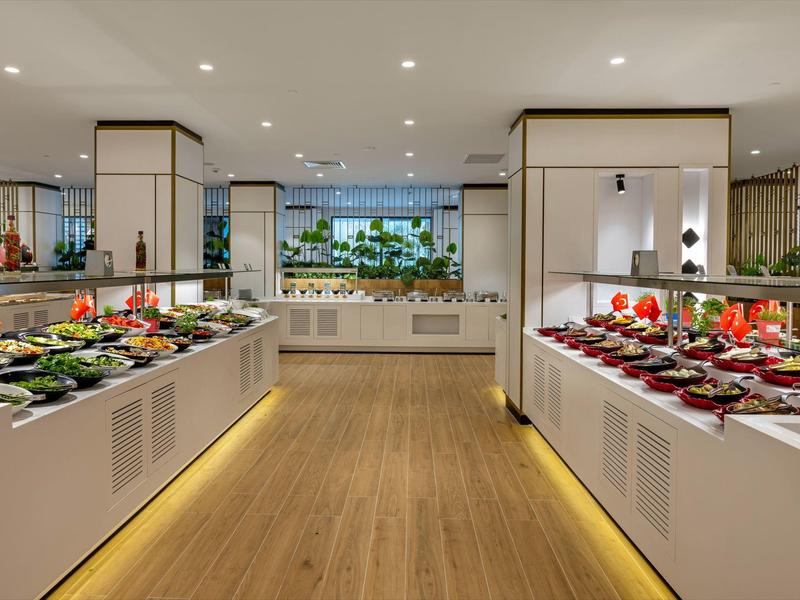 Estaciones de buffet modernas con variadas comidas en un restaurante luminoso con suelo de madera.