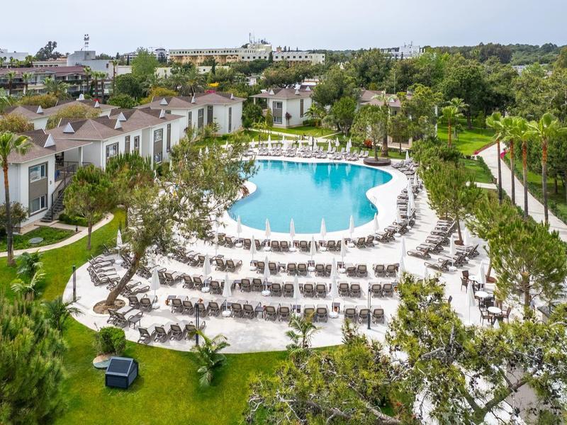 Gran piscina de hotel con tumbonas en un jardín verde y alojamientos alrededor.