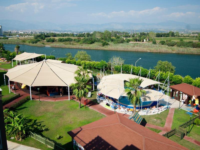 Área de piscina al aire libre junto a un lago con terrazas techadas y vegetación exuberante.