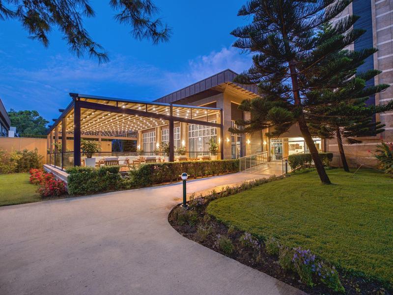 Hotel moderno al anochecer con pabellón iluminado y jardín cuidado.