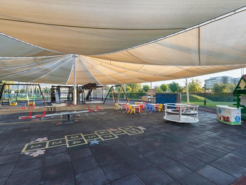 Zona de juegos cubierta con columpios y juegos sobre suelo de goma al aire libre.