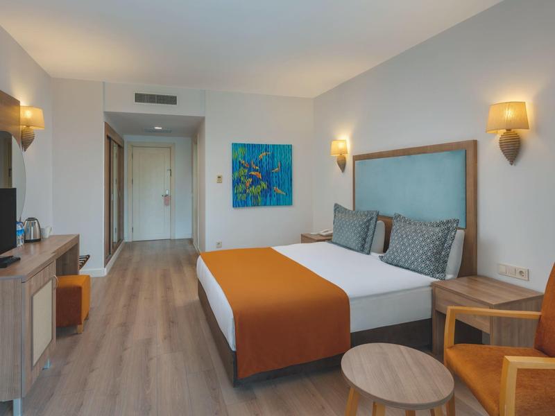 Habitación de hotel moderna con cama doble, área de estar, escritorio y mobiliario de madera clara.