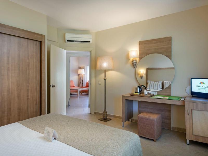 Habitación de hotel con cama, escritorio, espejo, TV, lámpara de pie y armario de madera.