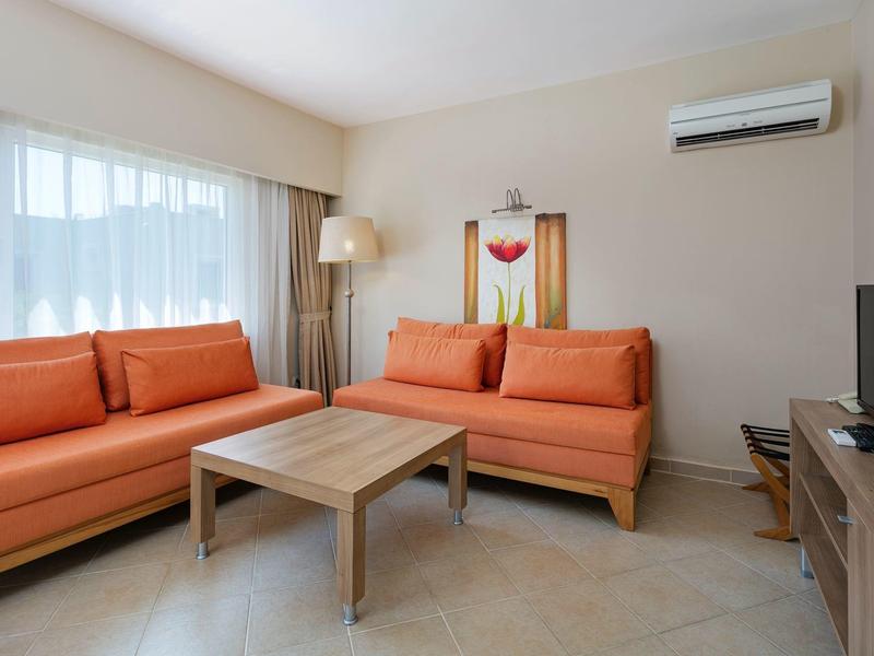 Sala luminosa con sofás naranjas, mesa de madera y TV en una habitación de hotel moderna.