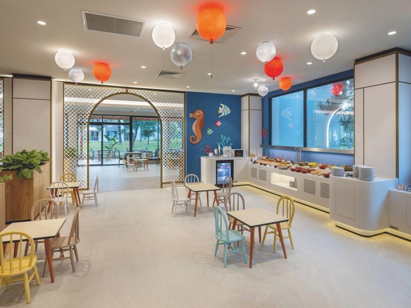 Sala de juegos infantil luminosa con muebles coloridos, decoraciones en la pared y ventana grande del hotel.