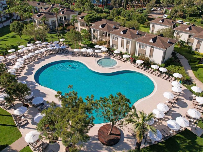 Gran piscina exterior curva rodeada de tumbonas blancas y sombrillas en un complejo hotelero.