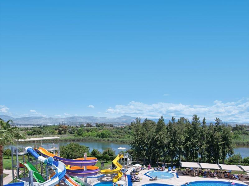 Gran piscina de hotel con toboganes coloridos y vista a un lago y montañas.