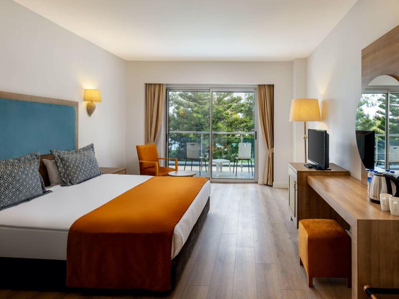 Habitación de hotel moderna con cama grande, escritorio y balcón con vista a los árboles.