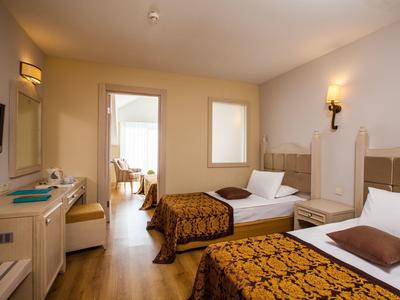 Hell eingerichtetes Hotelzimmer mit zwei Einzelbetten, braunen Decken und Holzboden.