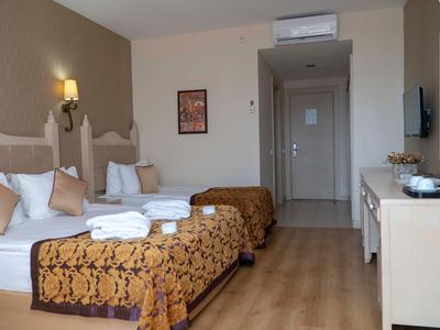 Hotelzimmer mit zwei Betten, braunen Decken, Holzboden und Möbeln, heller Beleuchtung und Klimaanlage.