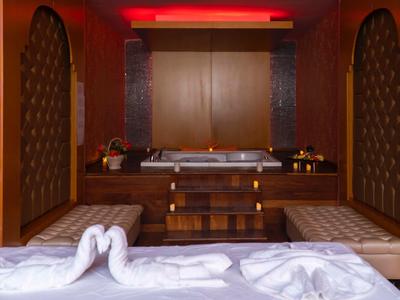 Eleganter Wellnessbereich mit zwei goldenen Badewannen, warmem Holz und roten Akzenten.
