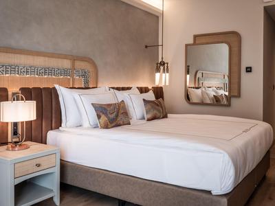 Habitación de hotel moderna con cama grande, ropa de cama blanca y acentos cálidos.