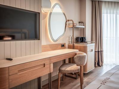 Área de trabajo moderna en habitación de hotel con escritorio de madera, silla y espejo junto a ventana con cortinas.
