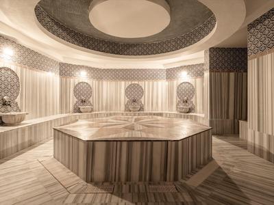 Baño turco lujoso con paredes de mármol y una piscina de agua caliente central.