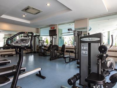 Fitnessraum mit Trainingsgeräten, blauem Boden, weißen Wänden und großen Spiegeln an der Wand.