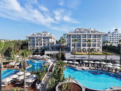 Hotel di lusso con due grandi piscine, lettini e verde sotto un cielo azzurro.