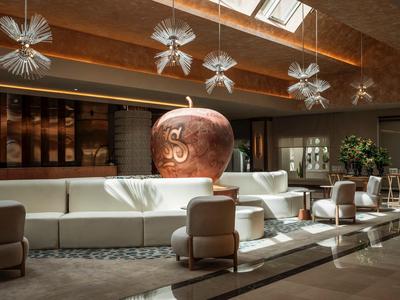 Lounge elegante dell'hotel con divano bianco, poltrone marroni e grandi lampade decorative.