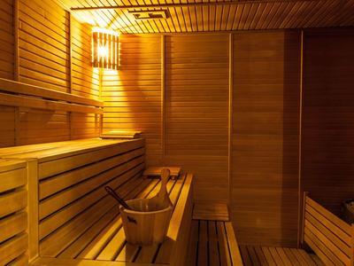 Innenraum einer Sauna mit hölzernen Bänken, Wänden und einem Wassereimer unter warmem Licht.