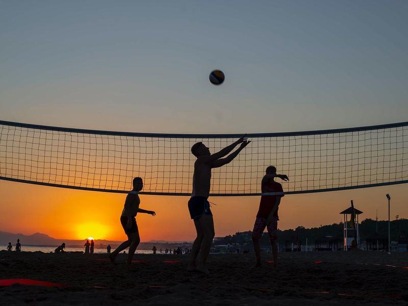 Trzy osoby grają w siatkówkę na plaży o zachodzie słońca.