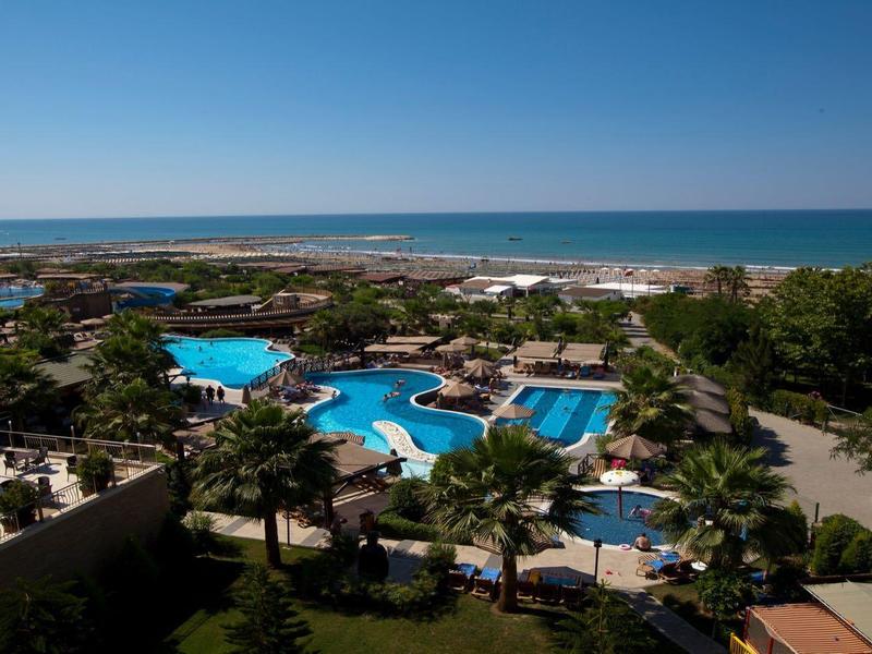 Widok na baseny hotelowe z morzem w tle w słoneczny dzień.
