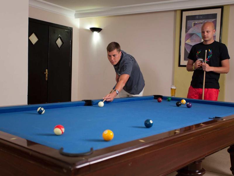 Deux hommes jouent au billard sur une table bleue à l'intérieur.