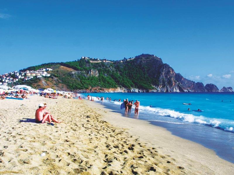 Plage avec rivage sablonneux, des gens et des falaises en arrière-plan sous un ciel bleu.