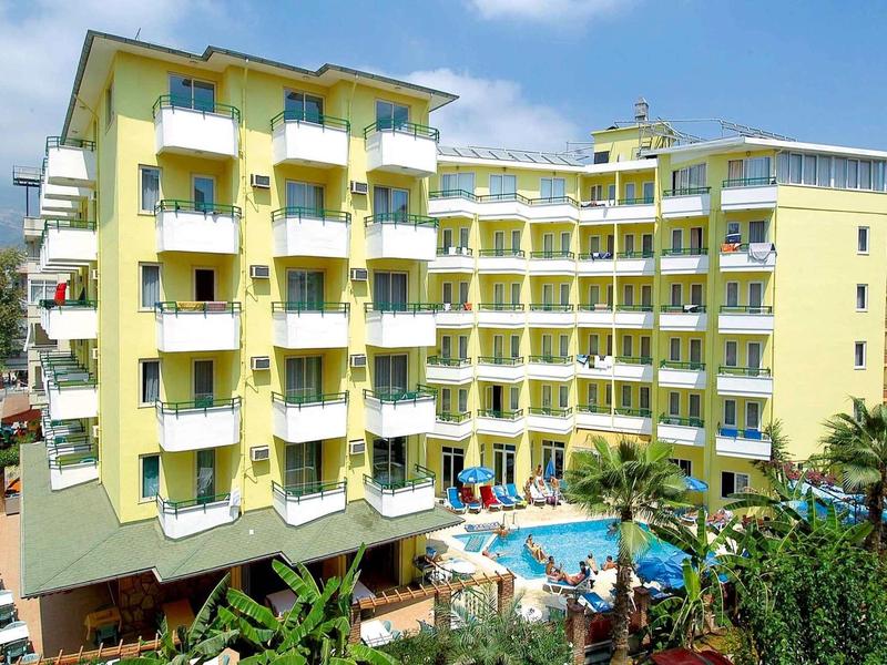 Hôtel jaune avec plusieurs balcons et une piscine dans la cour sous un ciel bleu.