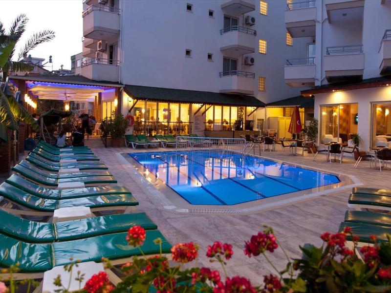 Vue extérieure en soirée d'une piscine d'hôtel éclairée avec chaises longues et fleurs de jardin.