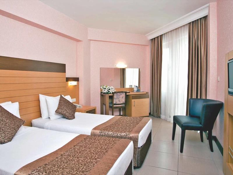 Chambre d'hôtel lumineuse avec deux lits simples, fauteuil, bureau et télévision.