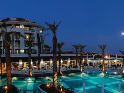 Großes Hotel mit beleuchteten Pools und Palmen, umgeben von Lichtern in der Abenddämmerung.