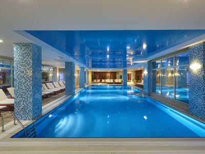 Moderner Innenpool mit blauer Decke, Mosaiksäulen und weißen Liegestühlen an der Seite.